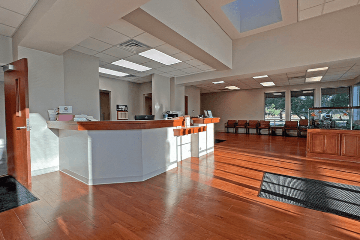 Waiting area with grey and blue chairs, a tv, and a reception desk in the back of the photo.